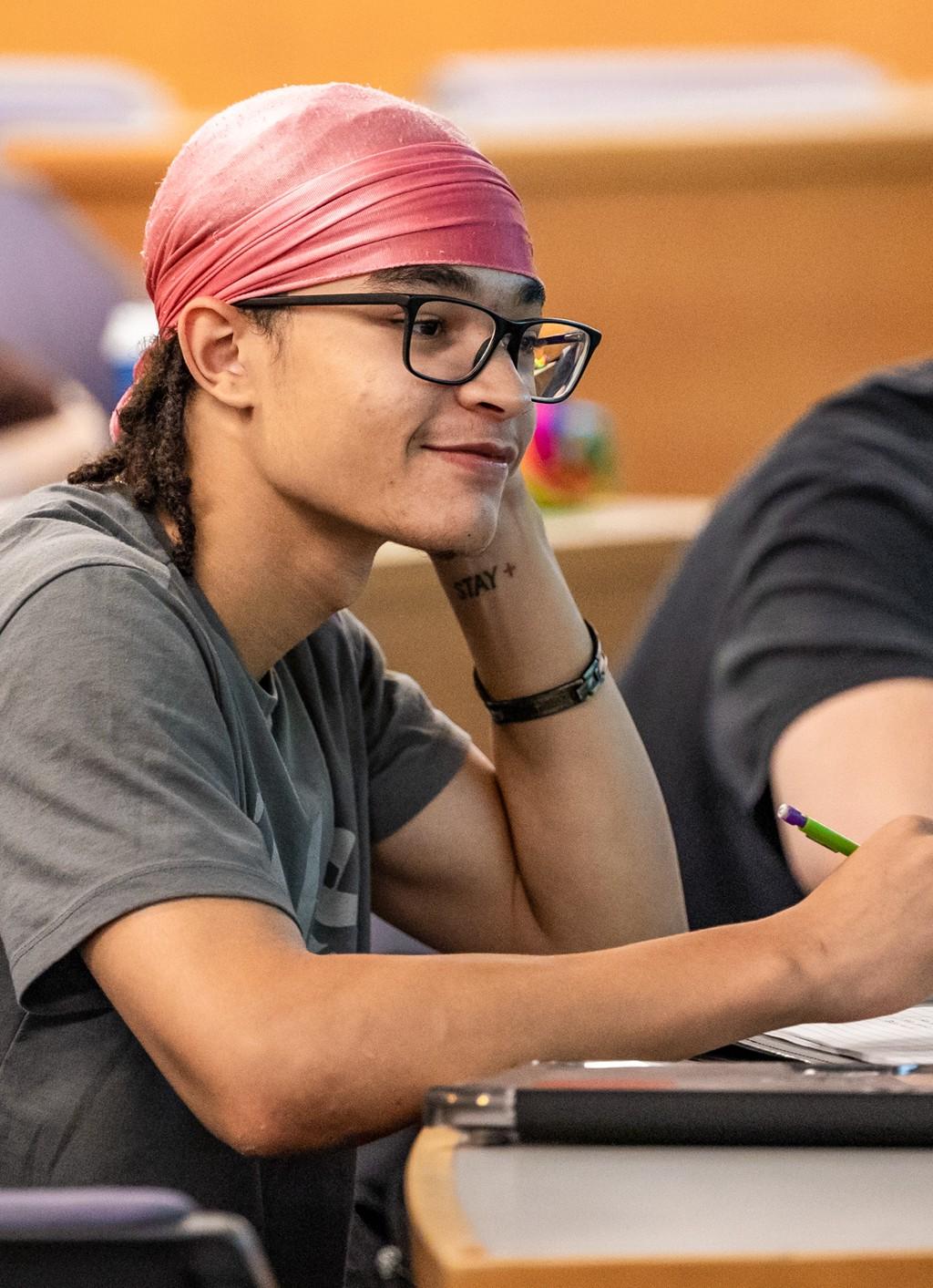 A student holds a pencil while listening to their professor during a lecture