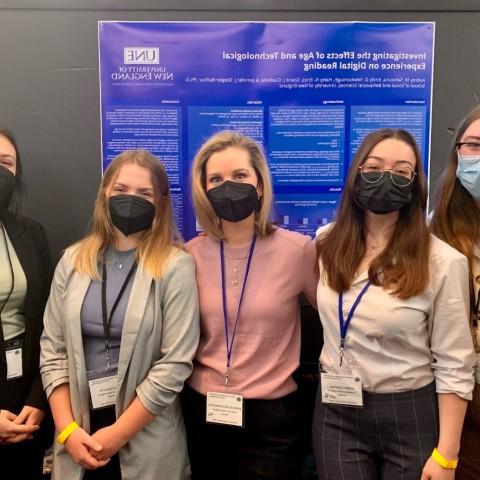 Photo of four students and faculty member standing in front of a poster they presented at a conference in New York City